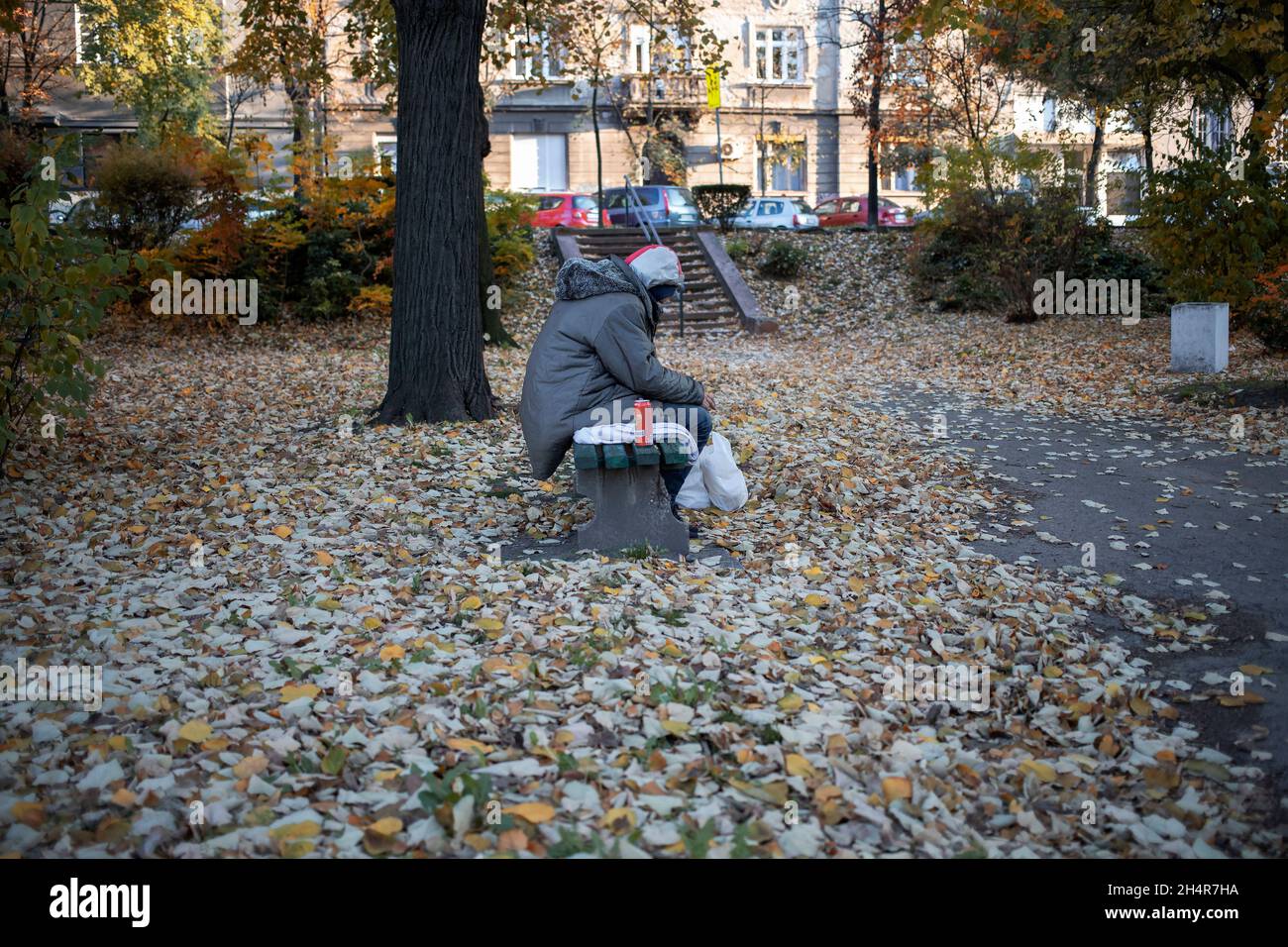 A hooded man sitting on a park bench next to a can of beer Stock Photo