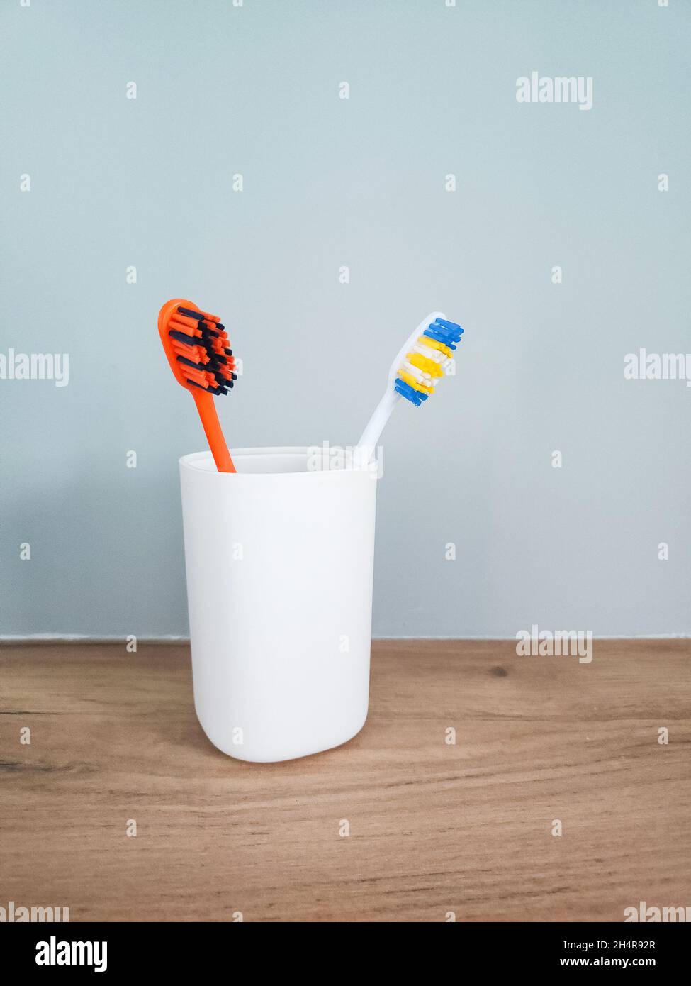 Two colored toothbrushes in white plastic glass on the shelf. Stock Photo