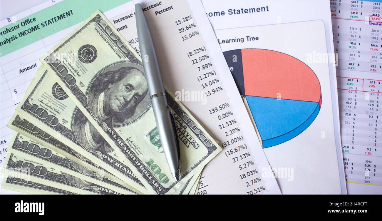 Stack of graphic financial reports, market analysis, pile of Ben Franklin 100 dollar bills and blue pen. Close-up graphs and charts. Concept image of Stock Photo