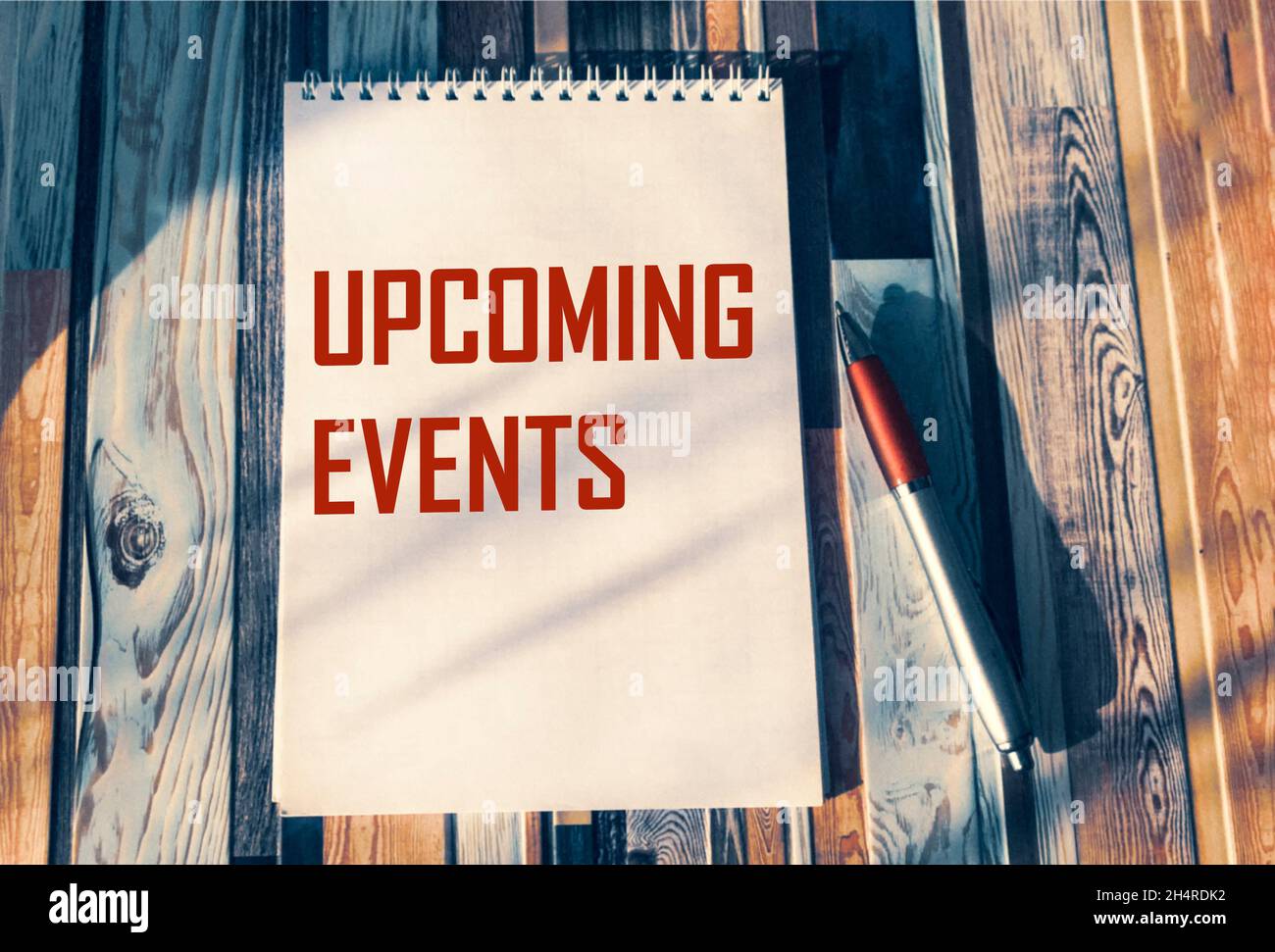 Concept message upcoming events on a notebook with a pen on a colored striped table. Stock Photo