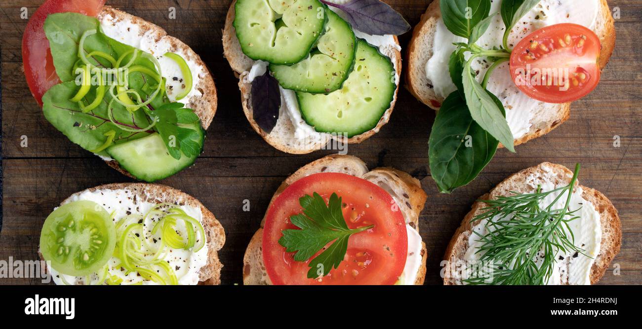 banner with various vegetable sandwiches with cream cheese, tomatoes, dill, cucumbers, leeks and basil. serving a vegetarian sandwiches for appetizers on cutting board. top view flat lay Stock Photo