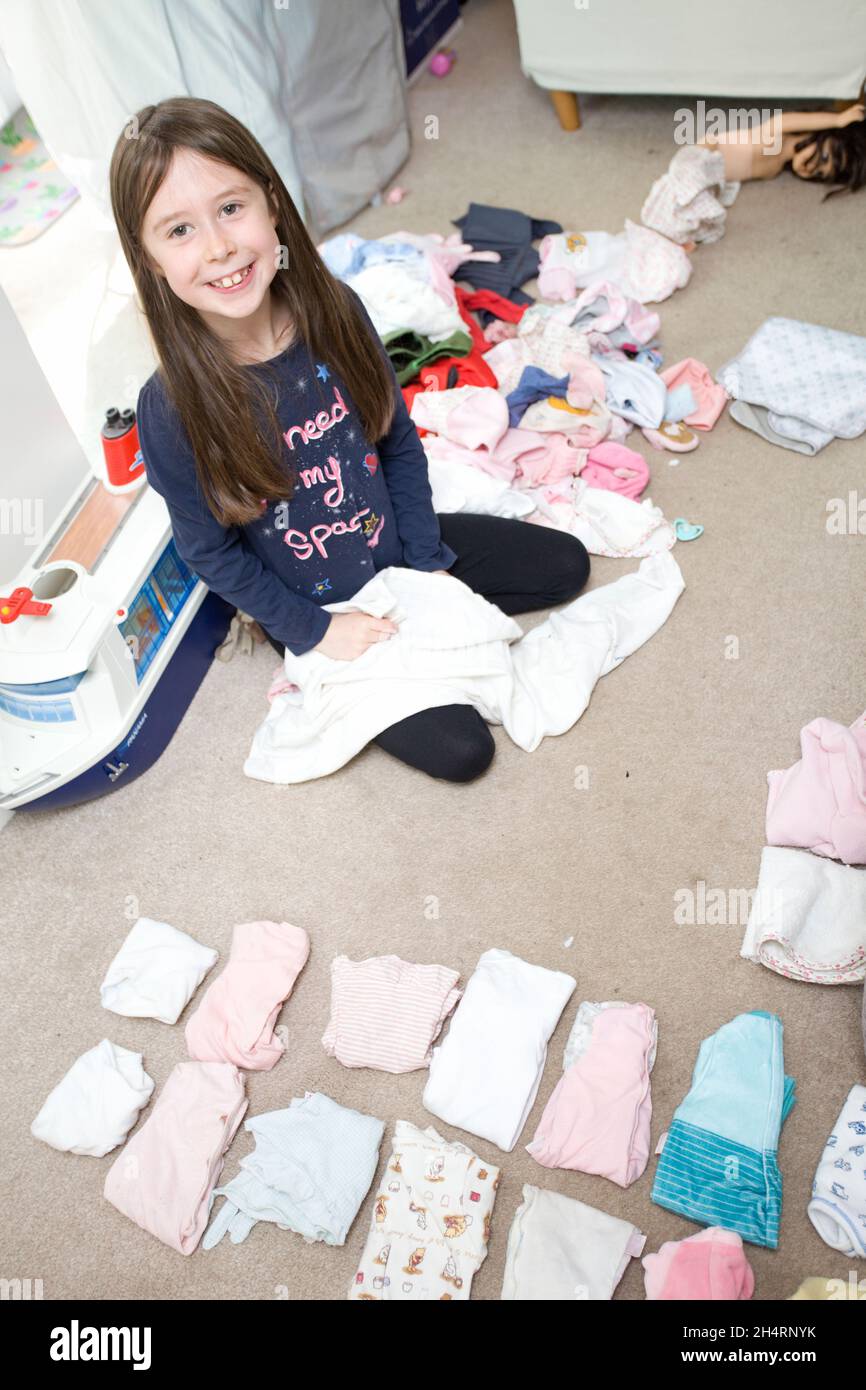 Young girl folding her dolls clothes. uk Stock Photo