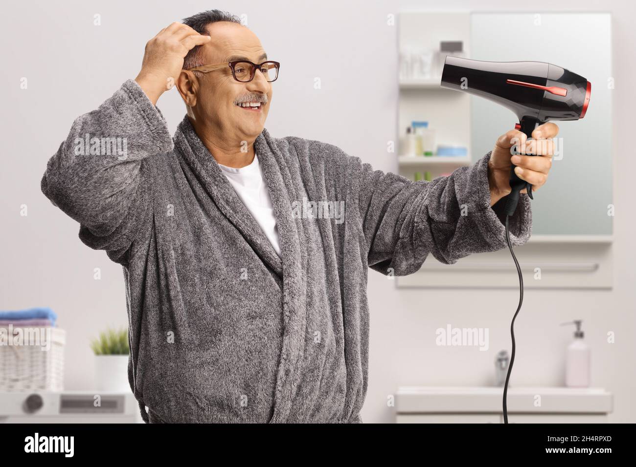 Happy mature man wearing a bathrobe and using a hair dryer in a bathroom Stock Photo