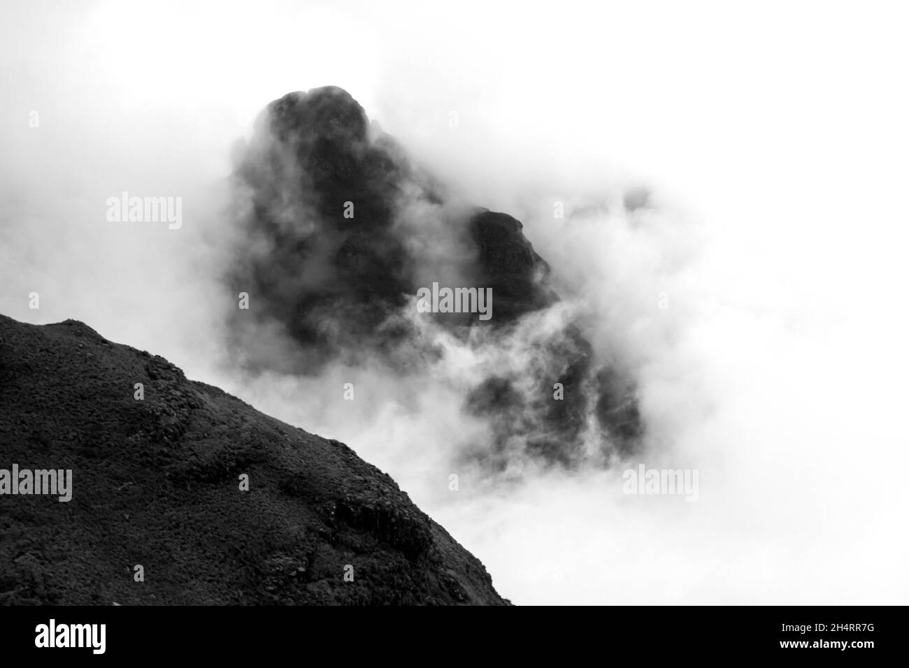 Black and white of a lone Mountain Peak, peeking out between the thick fog in the Drakensberg Mountains of South Africa, giving the illusion that it i Stock Photo