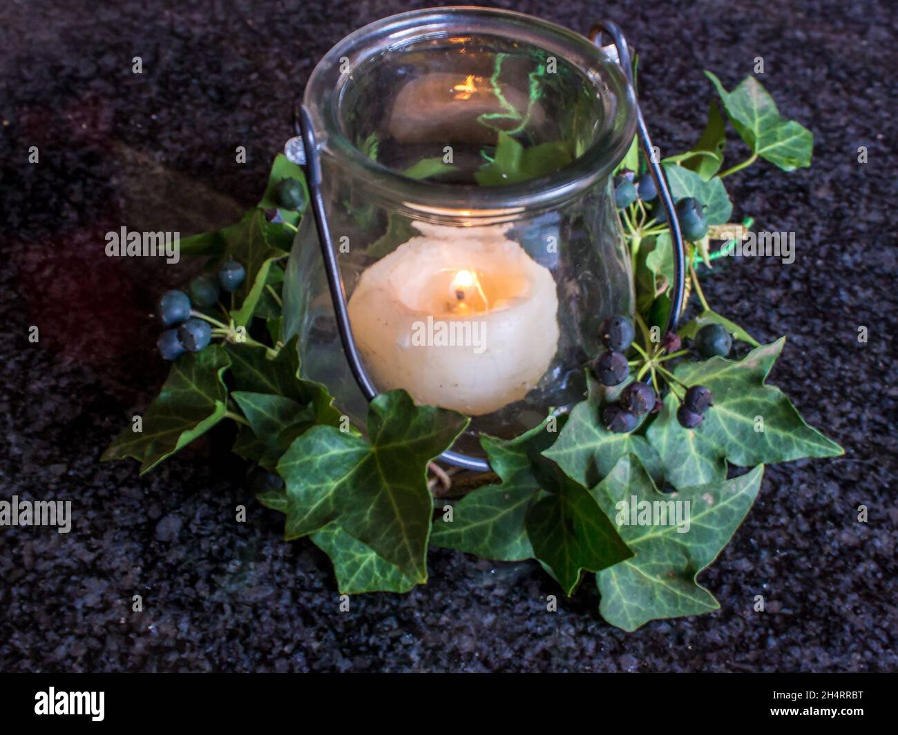 A small table decoration, consisting of a burning Candle of a burning candle surrounded by Ivy leaves and berries, against a dark background Stock Photo