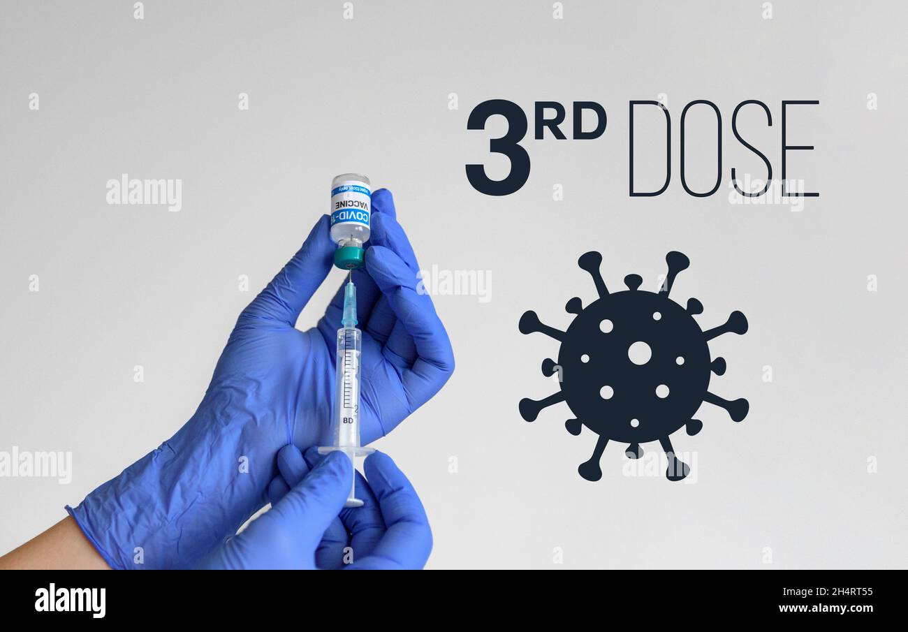 Medical worker holding covid syringe and vaccine in front of white background with 3rd dose text Stock Photo