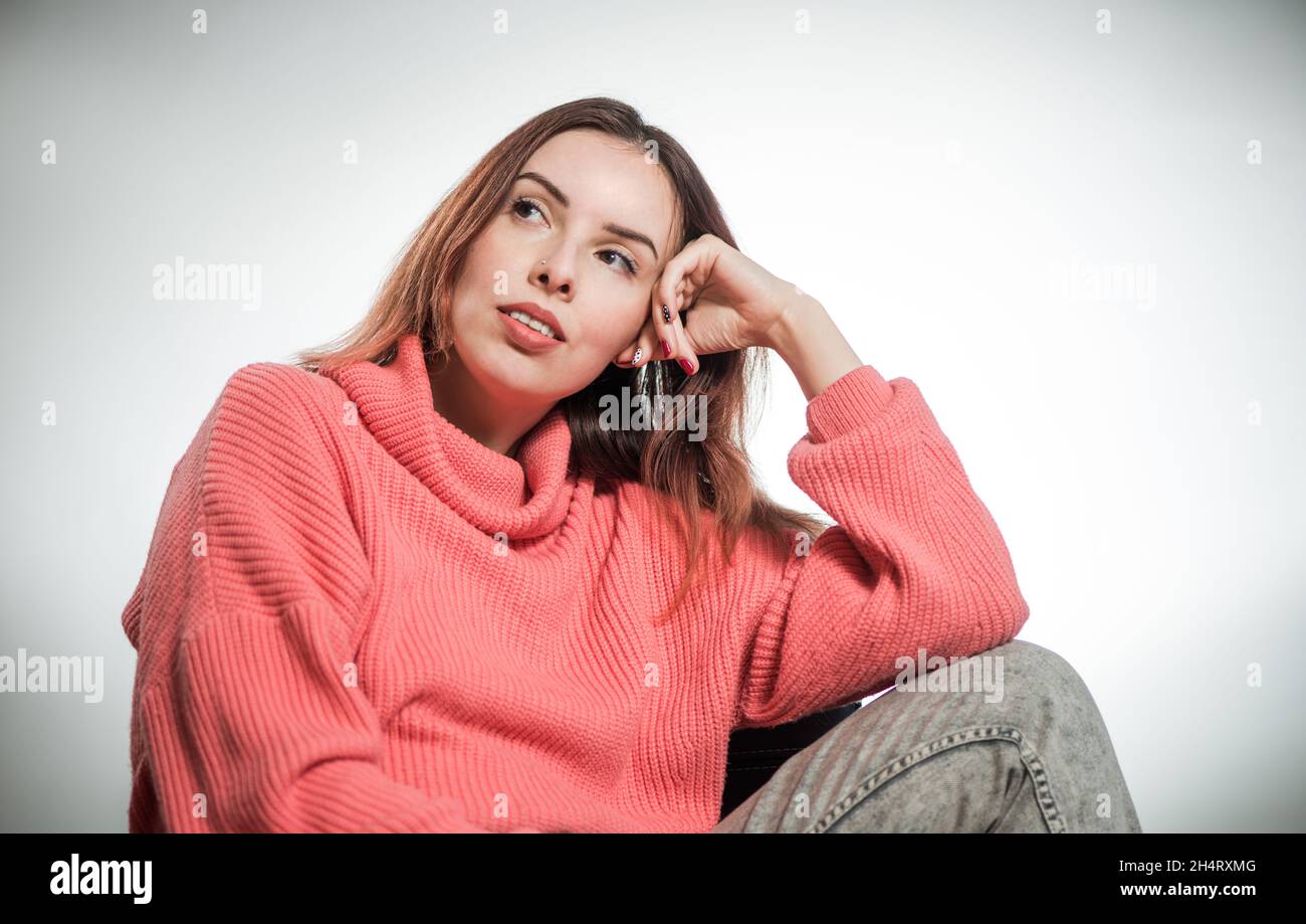 young thinking woman portrait in pink sweater on studio background Stock Photo
