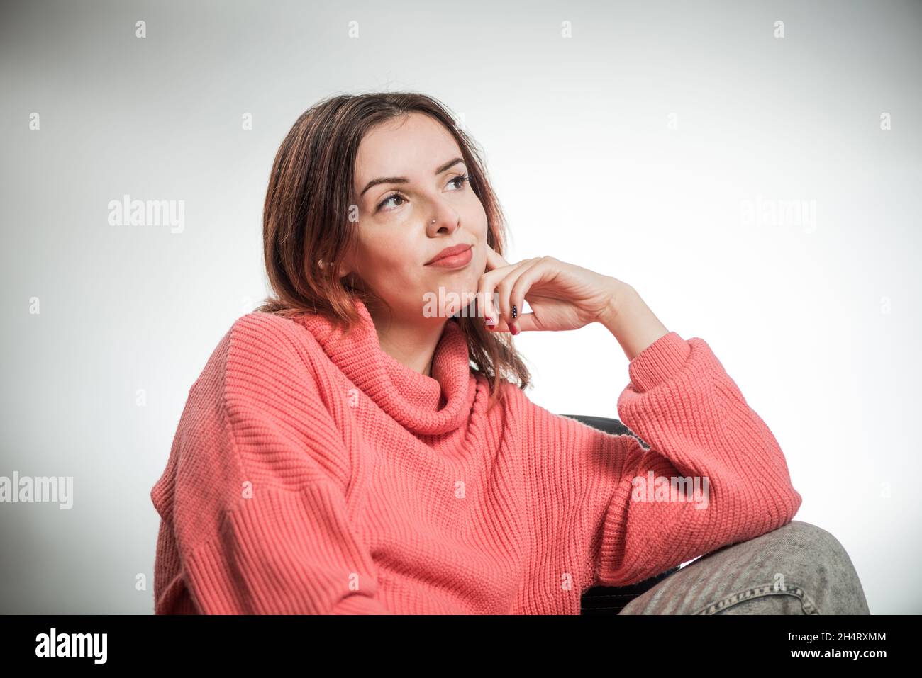 young thinking woman portrait in pink sweater on studio background Stock Photo