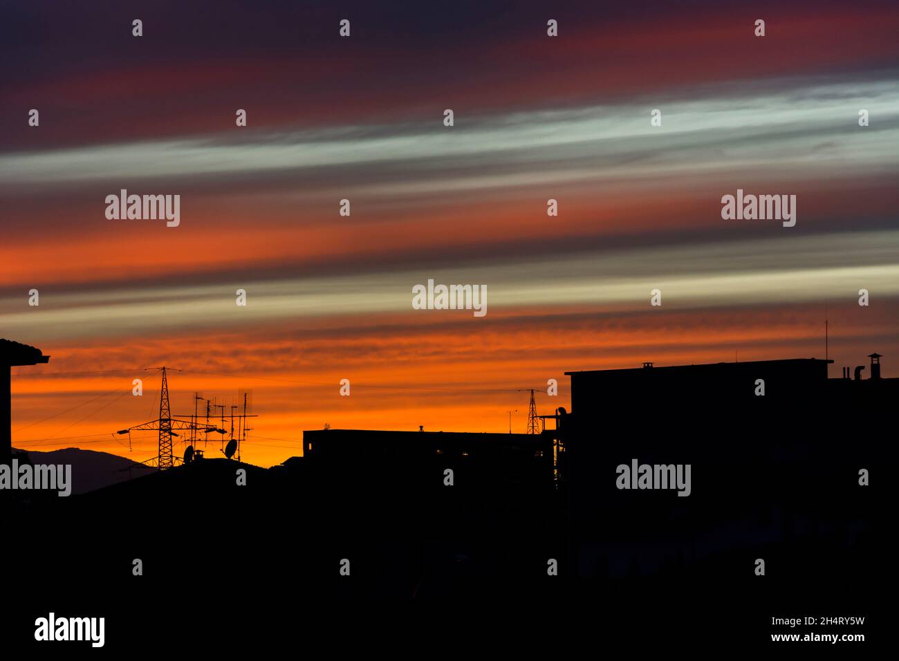 backlight silhouette of industrial city at sunset with striped sky after rain  grey clouds create many colors Stock Photo
