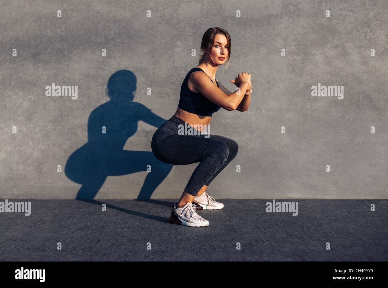 Image of a sportive woman, in sneakers and a tracksuit squatting, doing ...