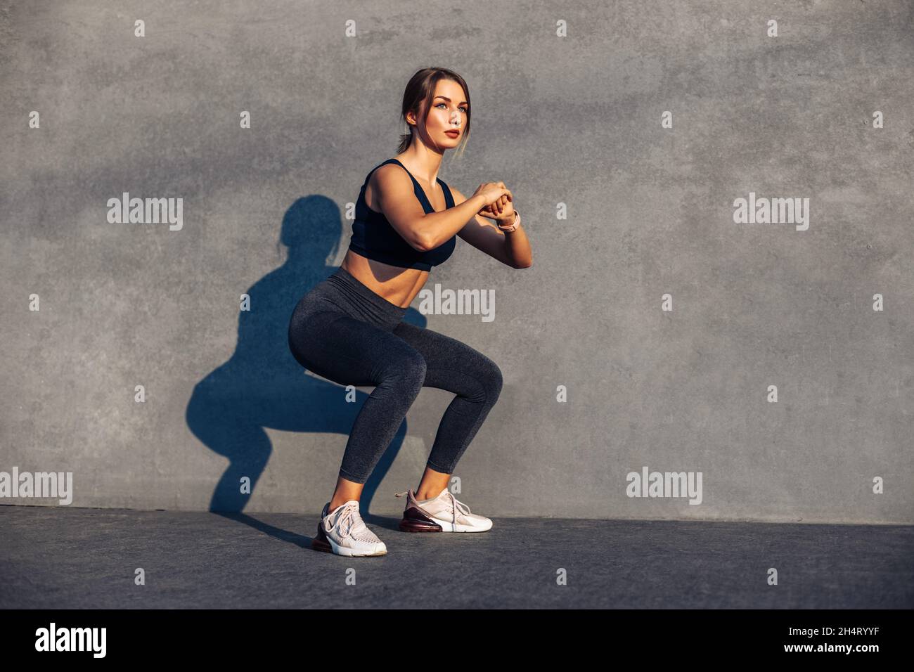 Image of a sportive woman, in sneakers and a tracksuit squatting, doing ...