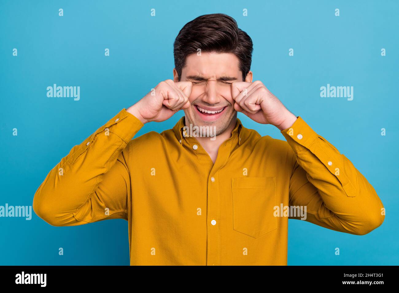 Photo of sad crying young guy dressed yellow shirt arms hands eyes isolated blue color background Stock Photo
