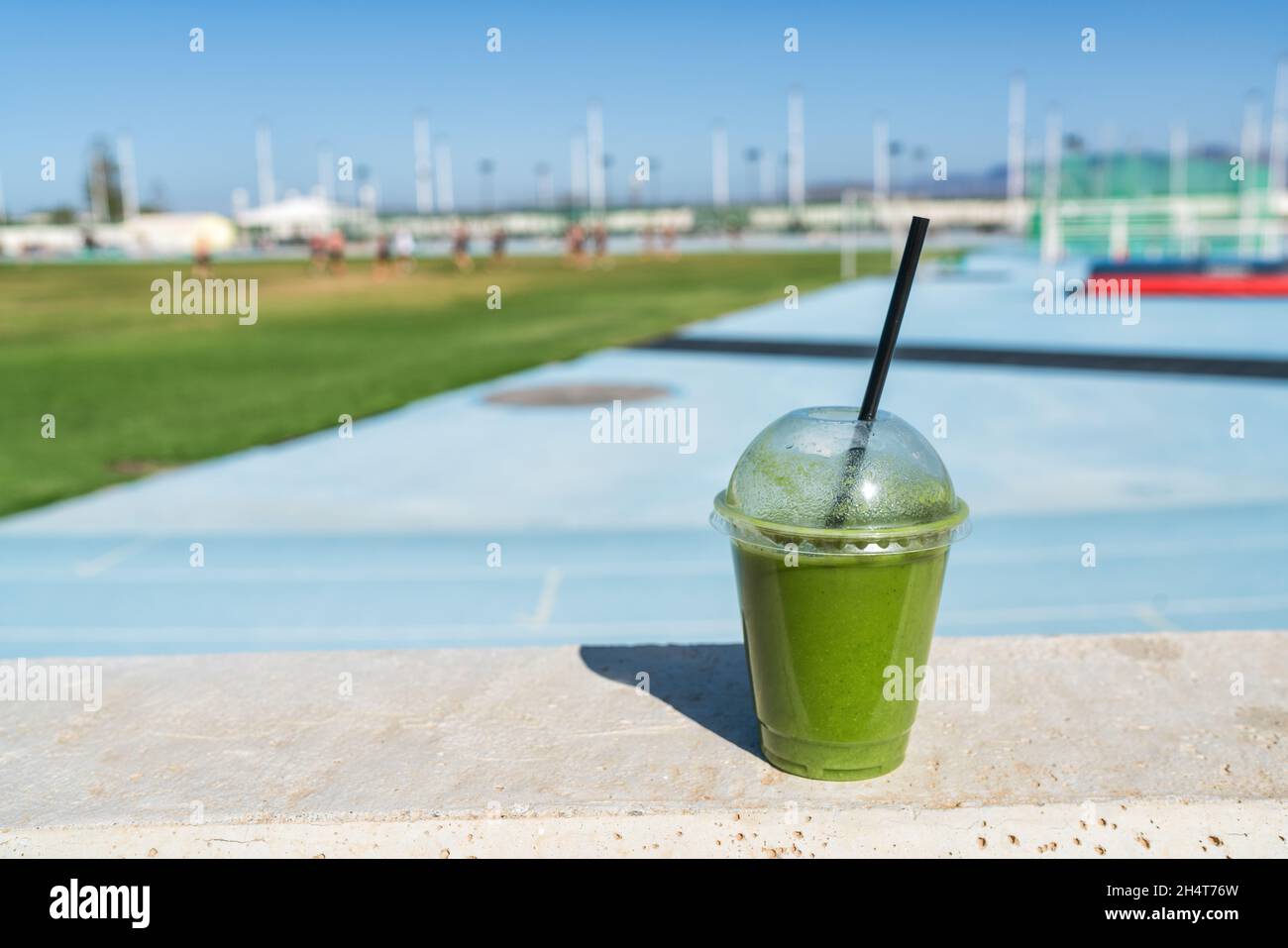 Green smoothie detox juice drink at outdoor sports stadium for runners athletes on blue running track. Healthy diet protein shake for sport people. Stock Photo
