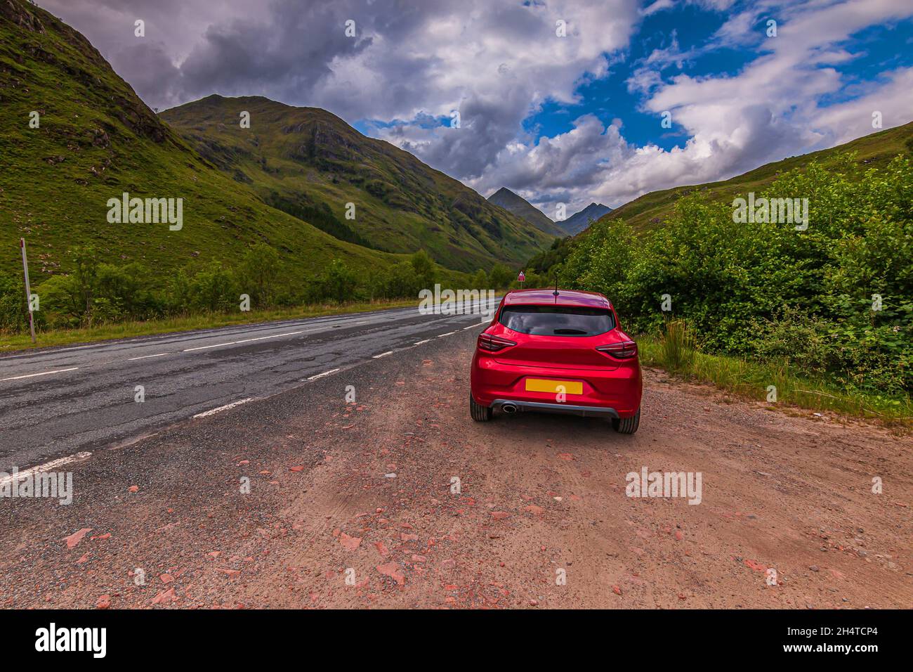Mountain range in the Scottish Highlands in summer. Mountains and hills in Scotland in sunshine. Red car in the foreground next to a road. Road throug Stock Photo