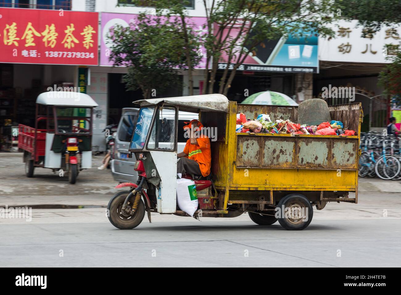 A three-wheeled utility vehicle collecting rubbish driving on the street in Yangshuo, China. Stock Photo