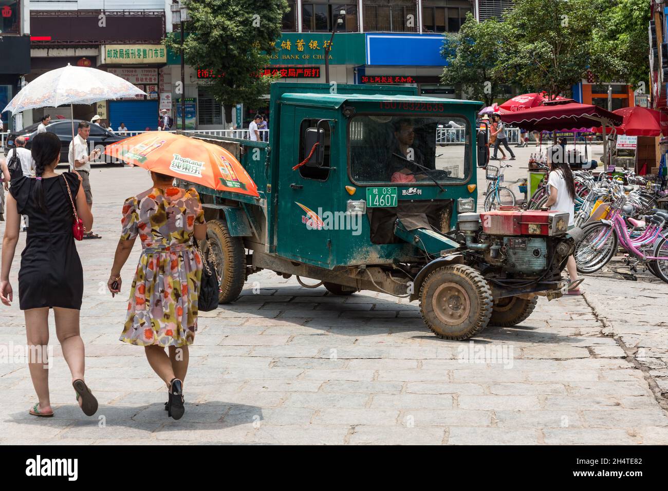 People walk by a Chinese utility vehicle on the street in Yangshuo, China. Stock Photo