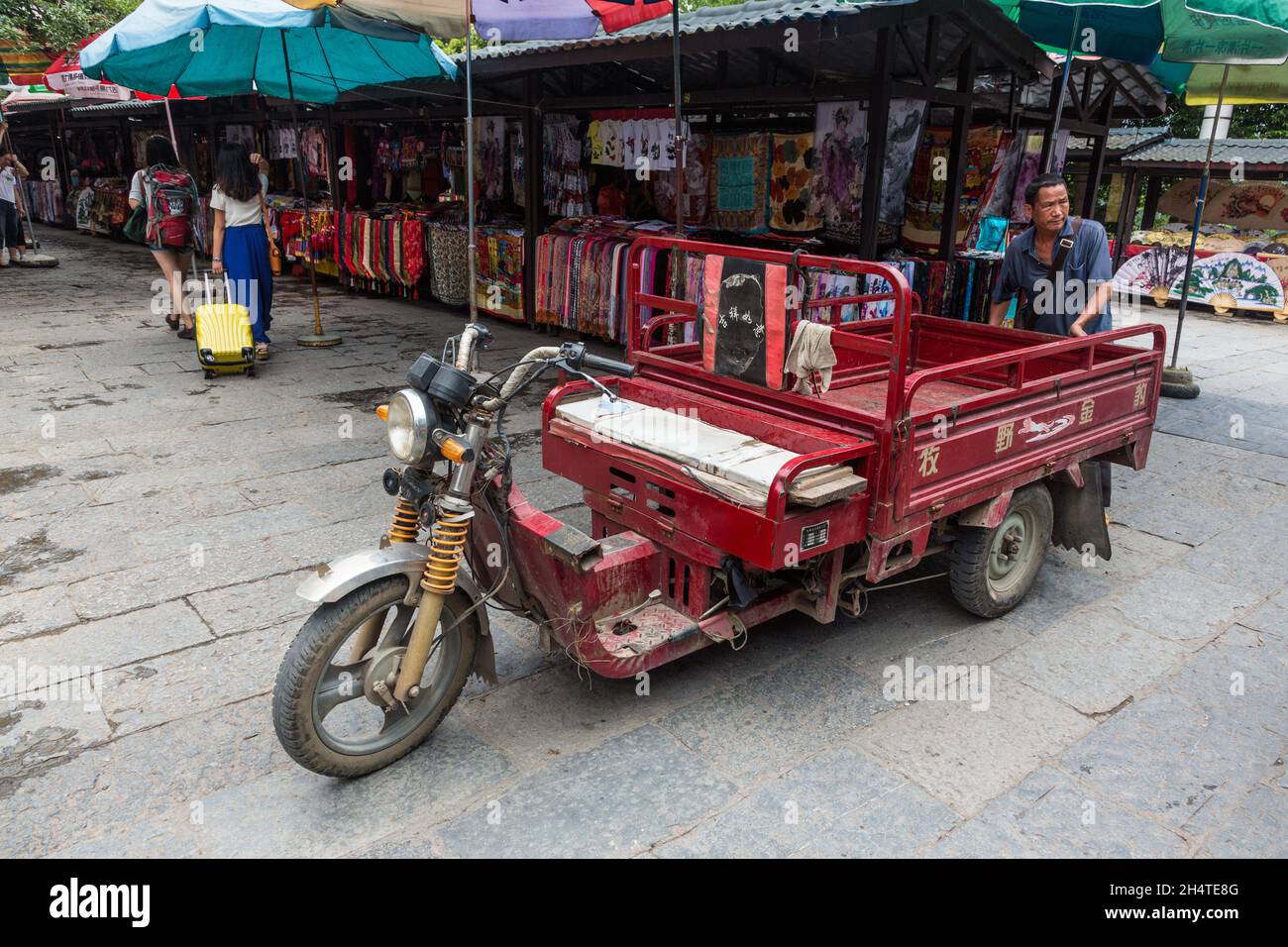 A Chinese man in the market with his three-wheeled untility goods-haulier vehicle in Yangshuo, China. Stock Photo