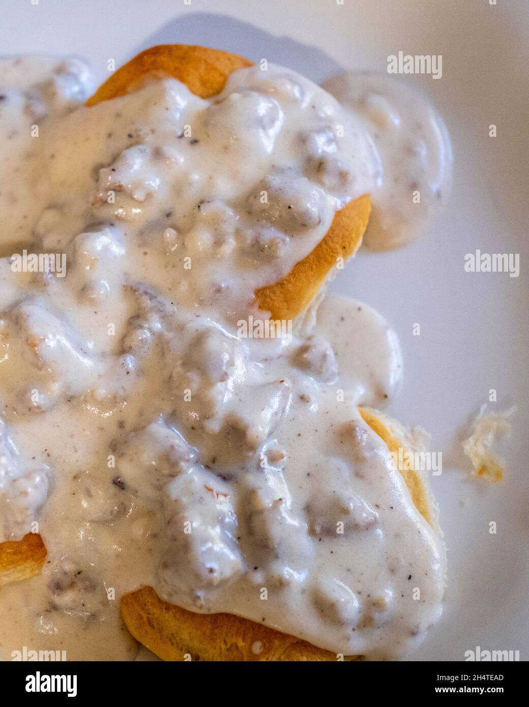 Sausage peppered milk gravy over biscuits on a white plate. Stock Photo