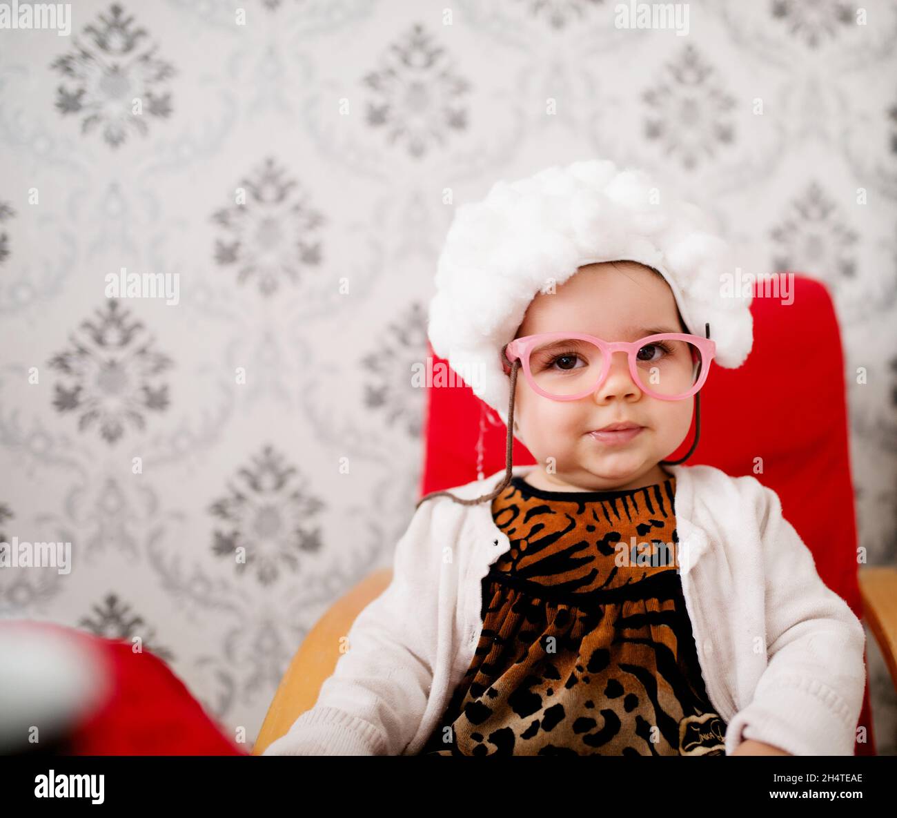 Cute baby girl sitting in a chair. Wearing granny costume with glasses