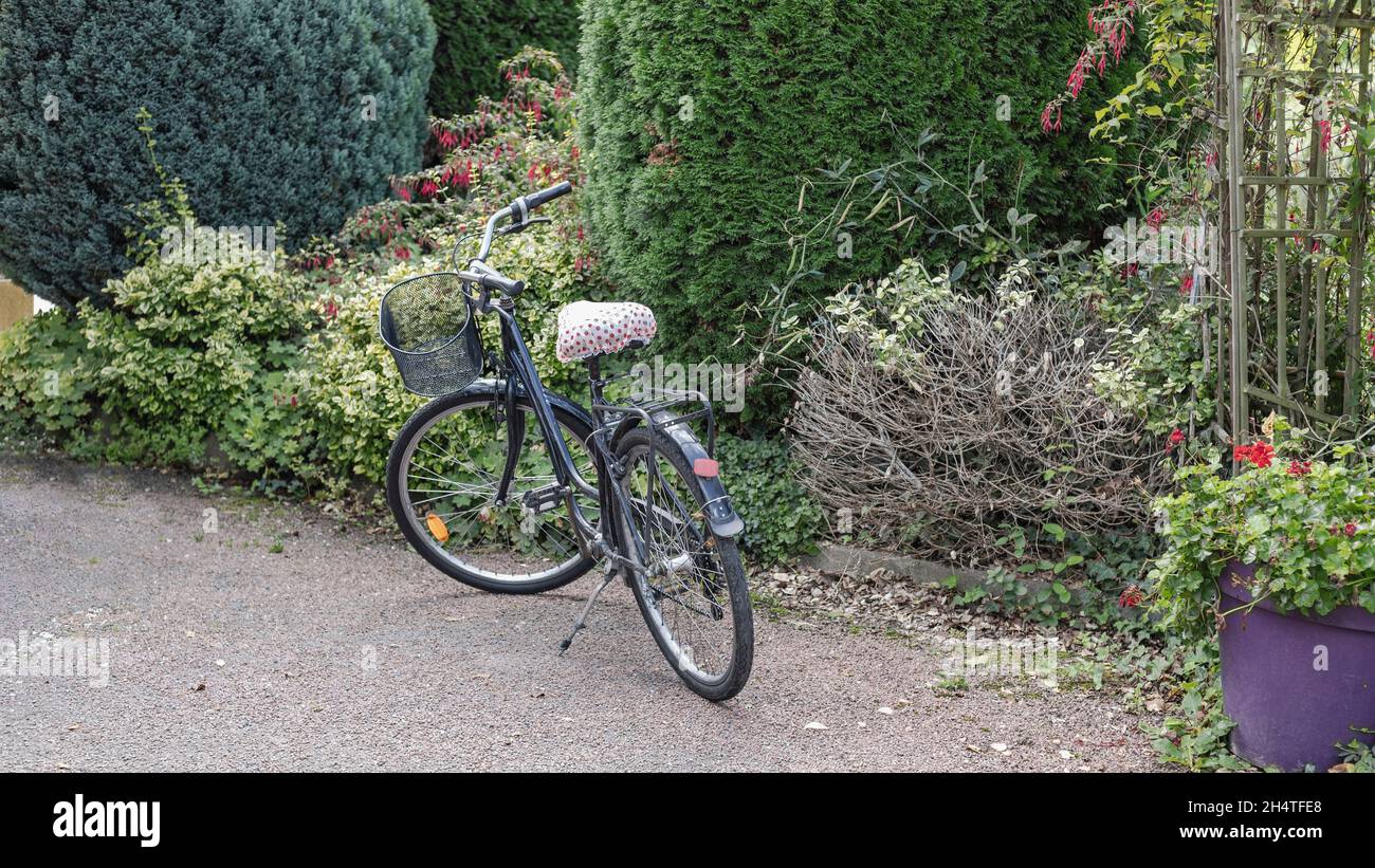 Blue bike stood in a garden with seat cover Stock Photo