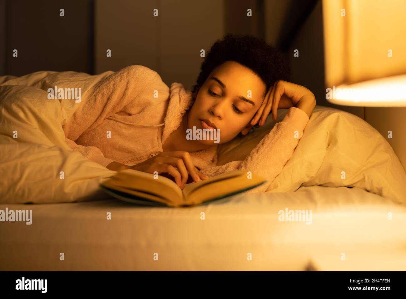 African American Woman Reading Book In Bed At Night Stock Photo