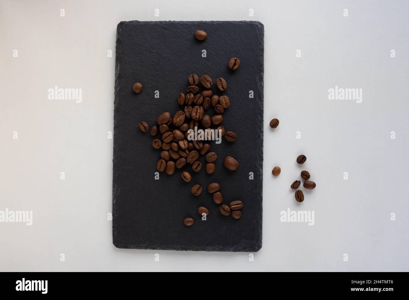 Coffee beans lie on a black plate on a white background. Stock Photo