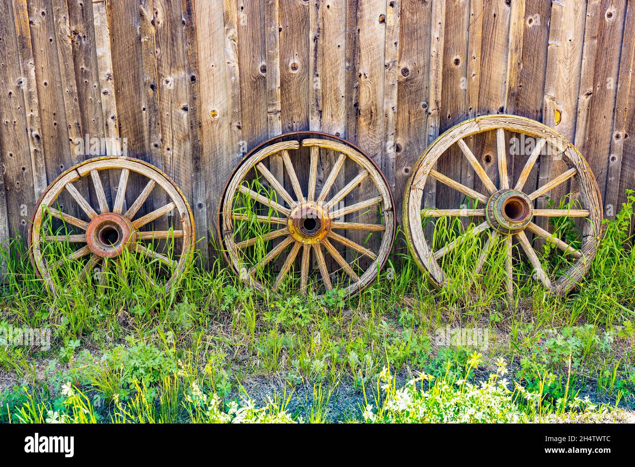 Three old weathered wooden wagon wheels against a barn wall Stock Photo