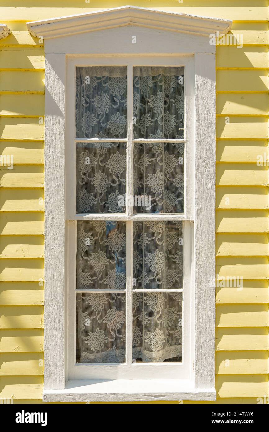 Exterior of old white painted window on bright yellow clapboard house Stock Photo