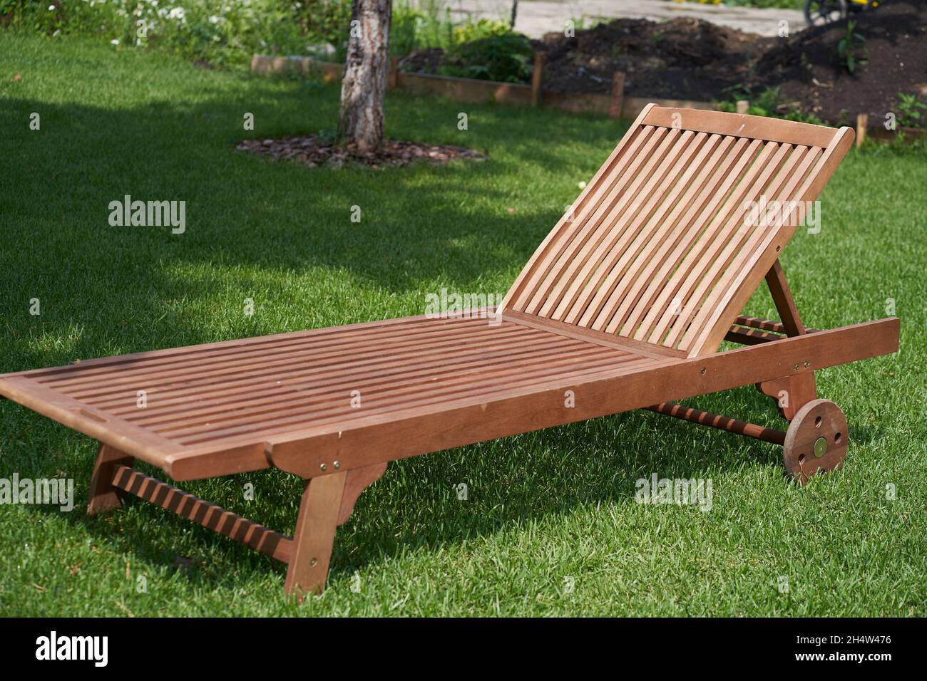 Wooden chaise longue in the fresh garden on the green grass. The shadow of a tree on the grass.The concept of recreation, tanning in the backyard. High quality photo Stock Photo