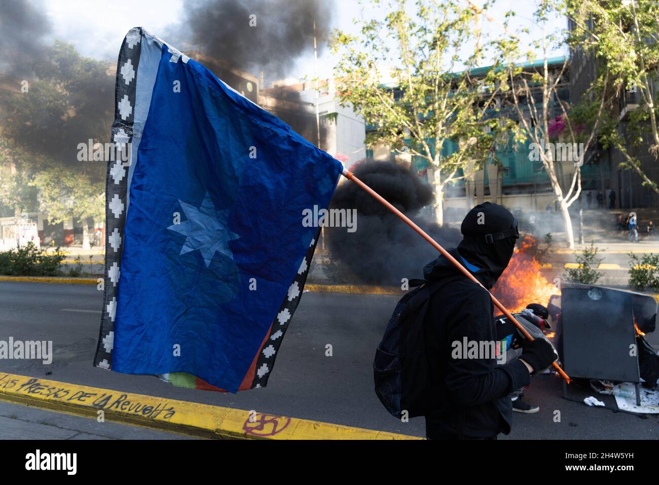 Santiago, Metropolitana, Chile. 4th Nov, 2021. A protester with a flag of the indigenous peoples walks in front of a barricade during protests against the government of Sebastian Pinera in Santiago, Chile. The protests come after the death of a Mapuche person during clashes in the southern region of Bio Bio after the Chilean government declared a state of emergency to reduce violence in that area of southern Chile. (Credit Image: © Matias Basualdo/ZUMA Press Wire) Stock Photo