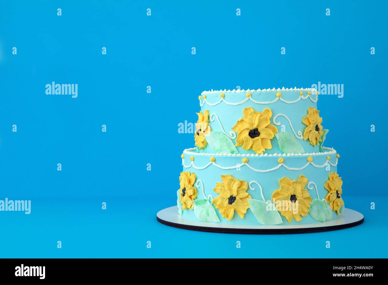 Two-tiered cake for a little girl princess with yellow flowers on blue background like a cartoon Beautiful sunflower decorated cake Stock Photo