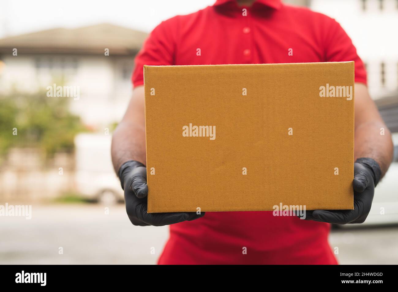 Postman in red wearing glove uniform holding package Stock Photo - Alamy