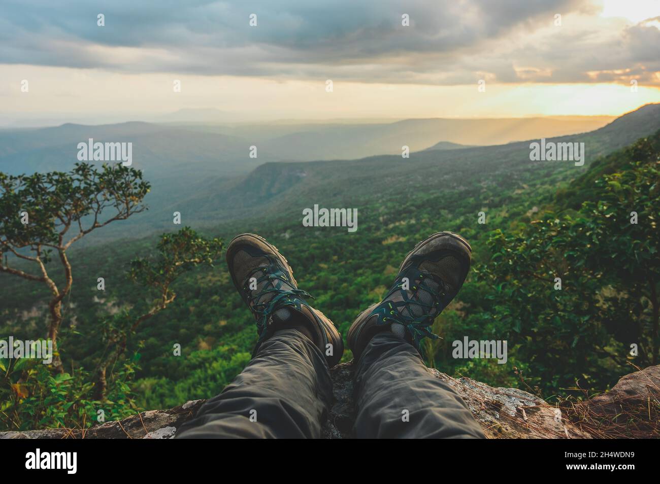 The hiker climbed, rested, and held his feet off the edge of the cliff. Stock Photo