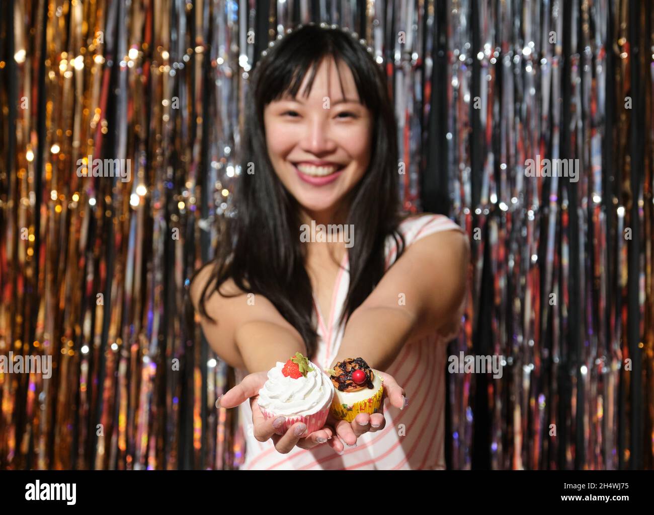 Young asian woman show cupcakes to the camera over a party background. Stock Photo