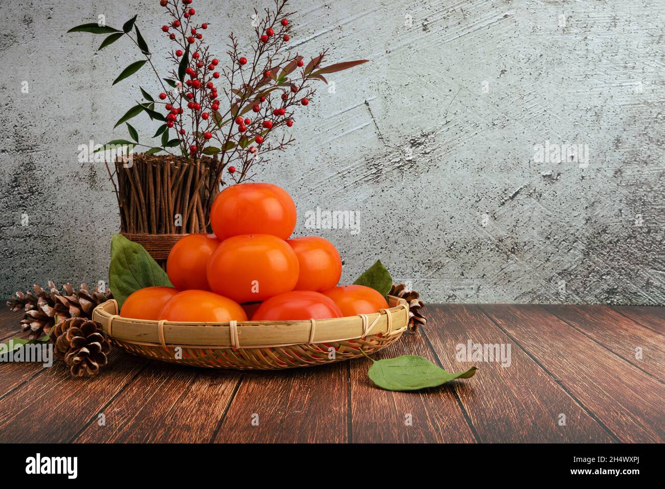 Ripe persimmons in a bamboo basket. Persimmon set front view, horizontal wooden table background. Stock Photo
