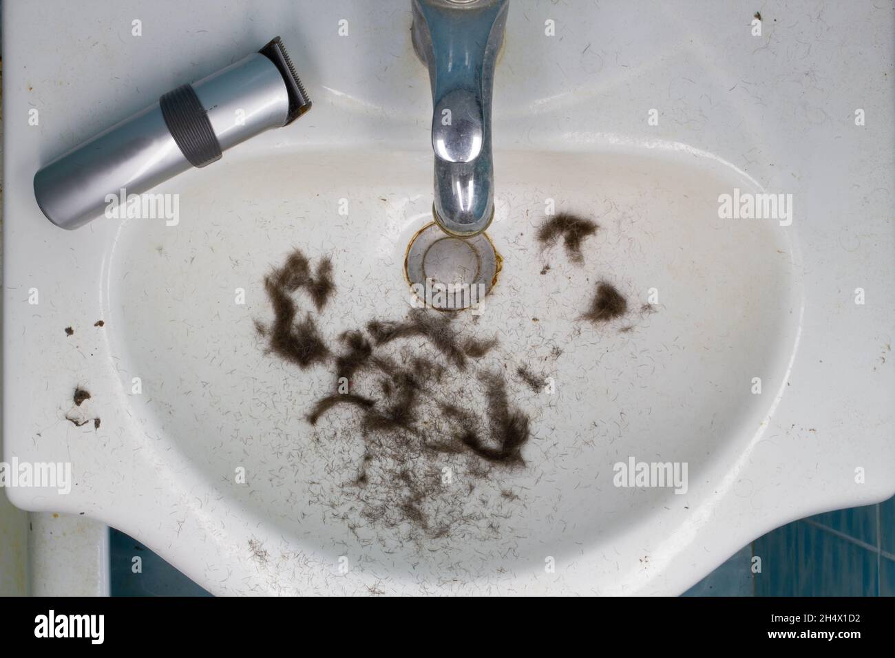 Dirty Bathroom sink with hair after shaving and wireless electric razor.  Freshly cut hair from the head, beard and mustache. Water Mixer Tap. Clogged Stock Photo