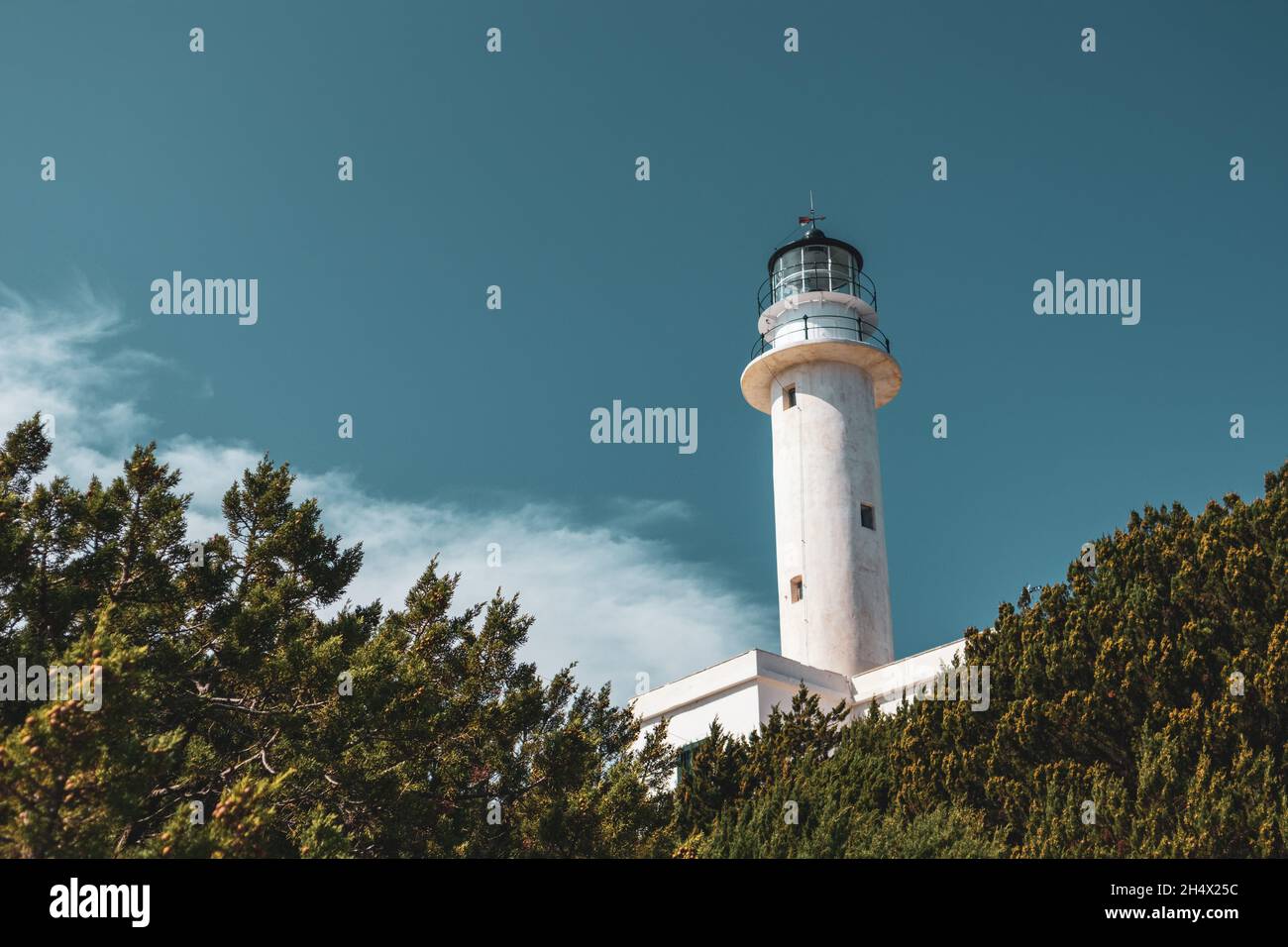 White lighthouse tall tower in greenery on a bright clear blue sky in Greece, Ionian sea. Scenic travel destination. Lefkada island. Color graded Stock Photo