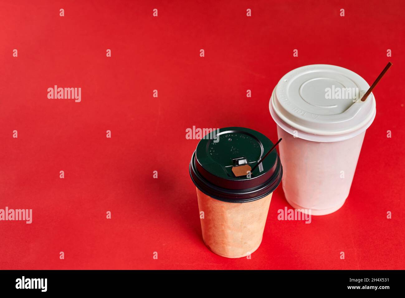 Two singleuse plastic coffee cups on red background with copy space