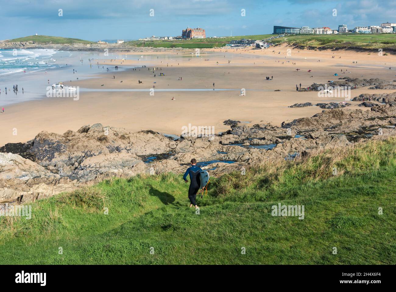 A surfer carrying his surfboard walking down a footpath to Fistral Beach at low tide in Newquay in Cornwall. Stock Photo