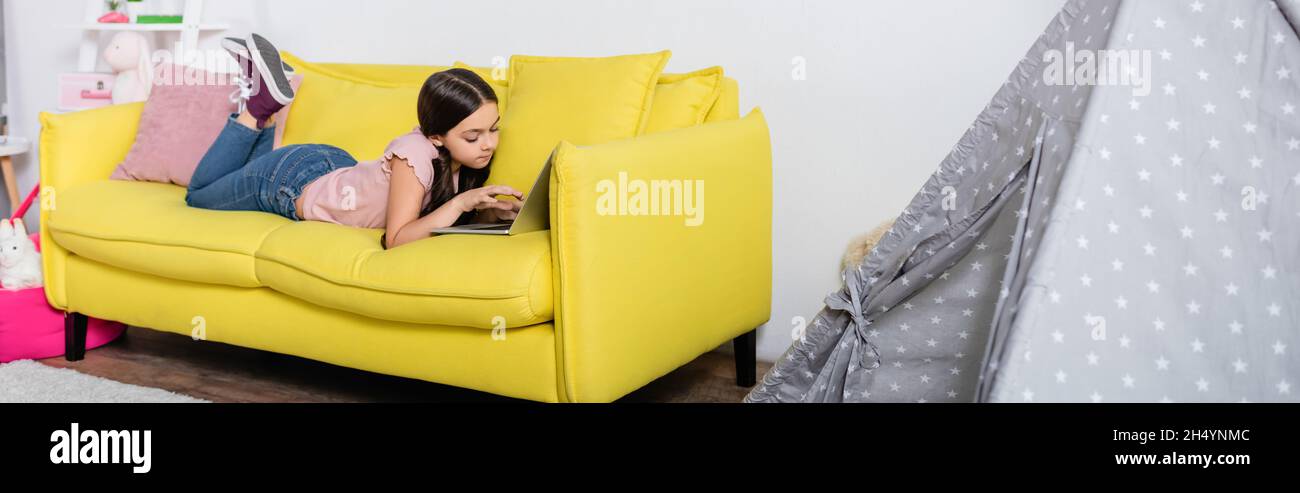 preteen girl lying on couch and using laptop in modern living room ...