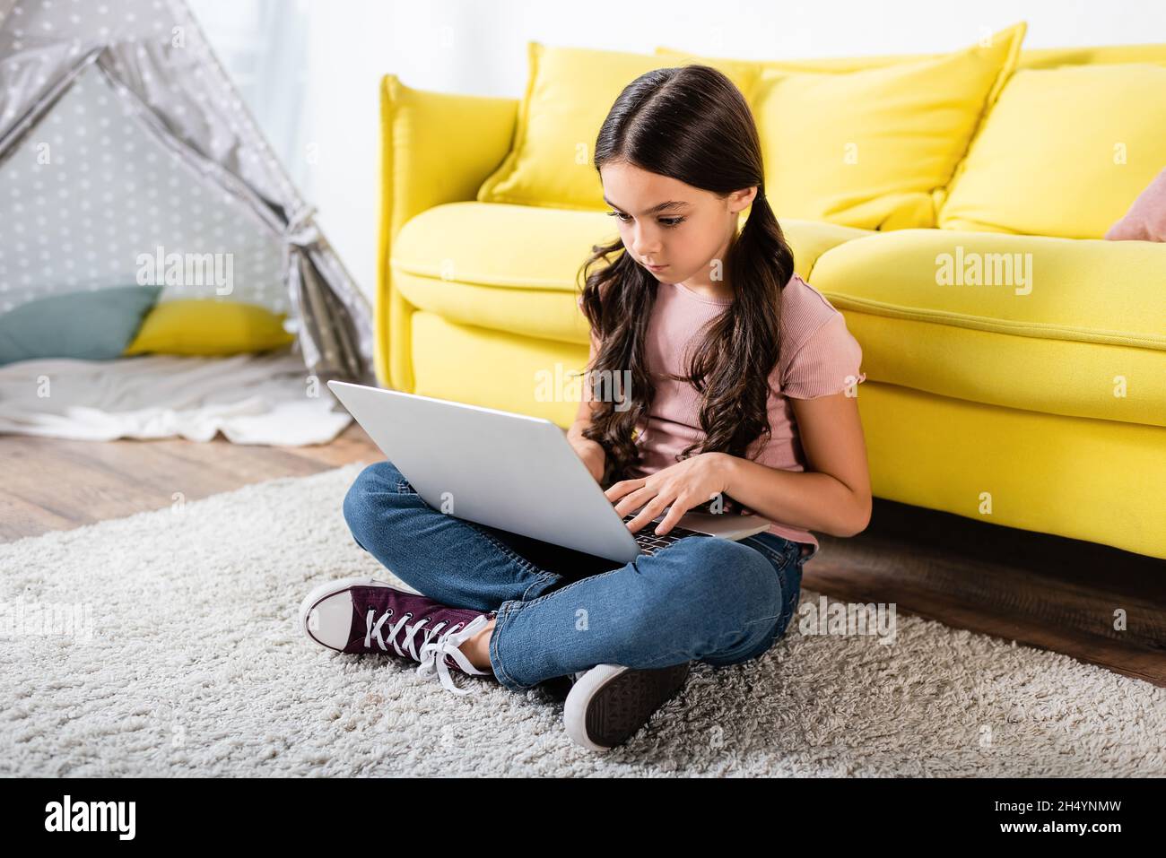 preteen girl sitting on carpet and using laptop in modern living room ...