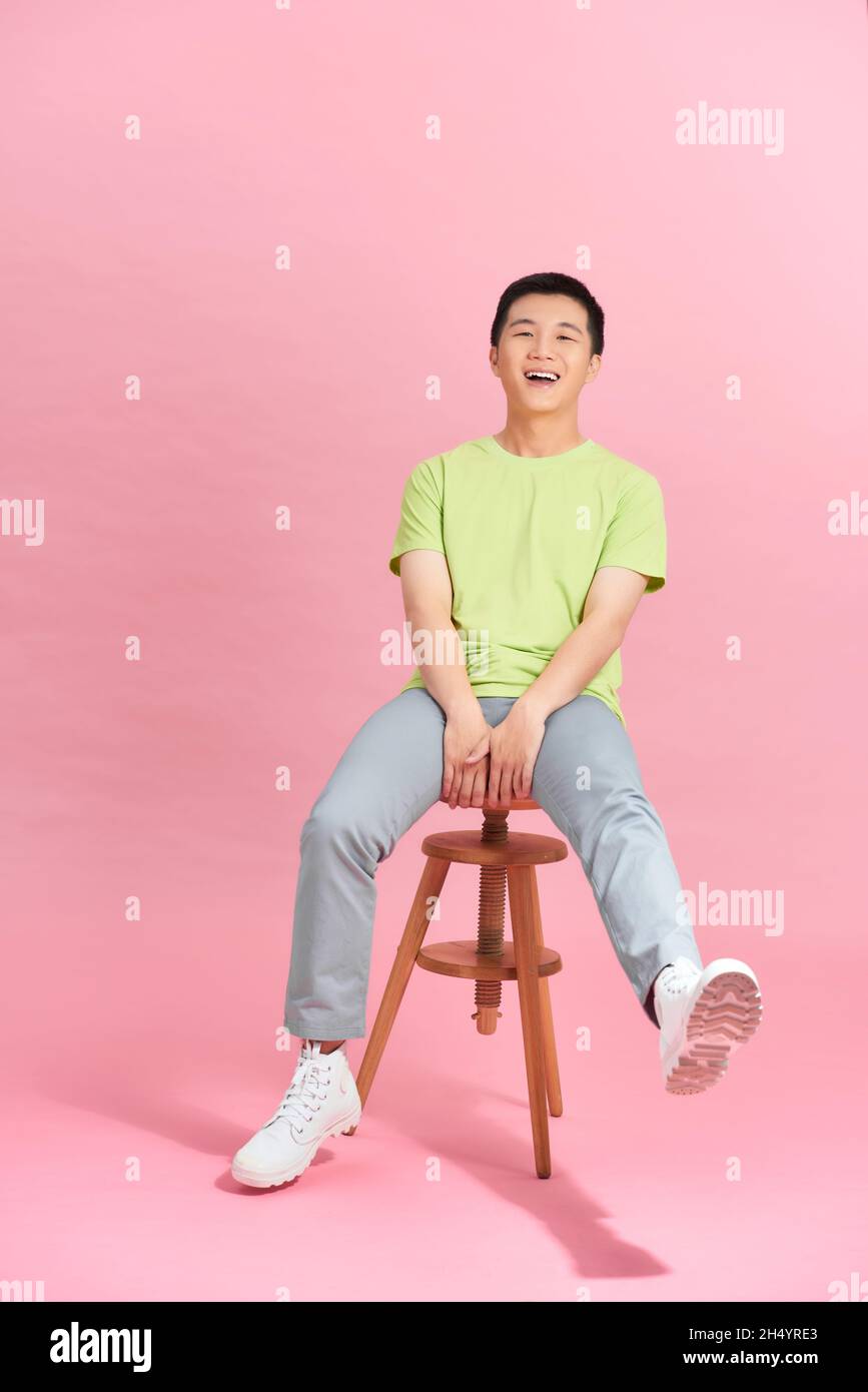 A young man in a white T-shirt is sitting on a high chair. Stock Photo