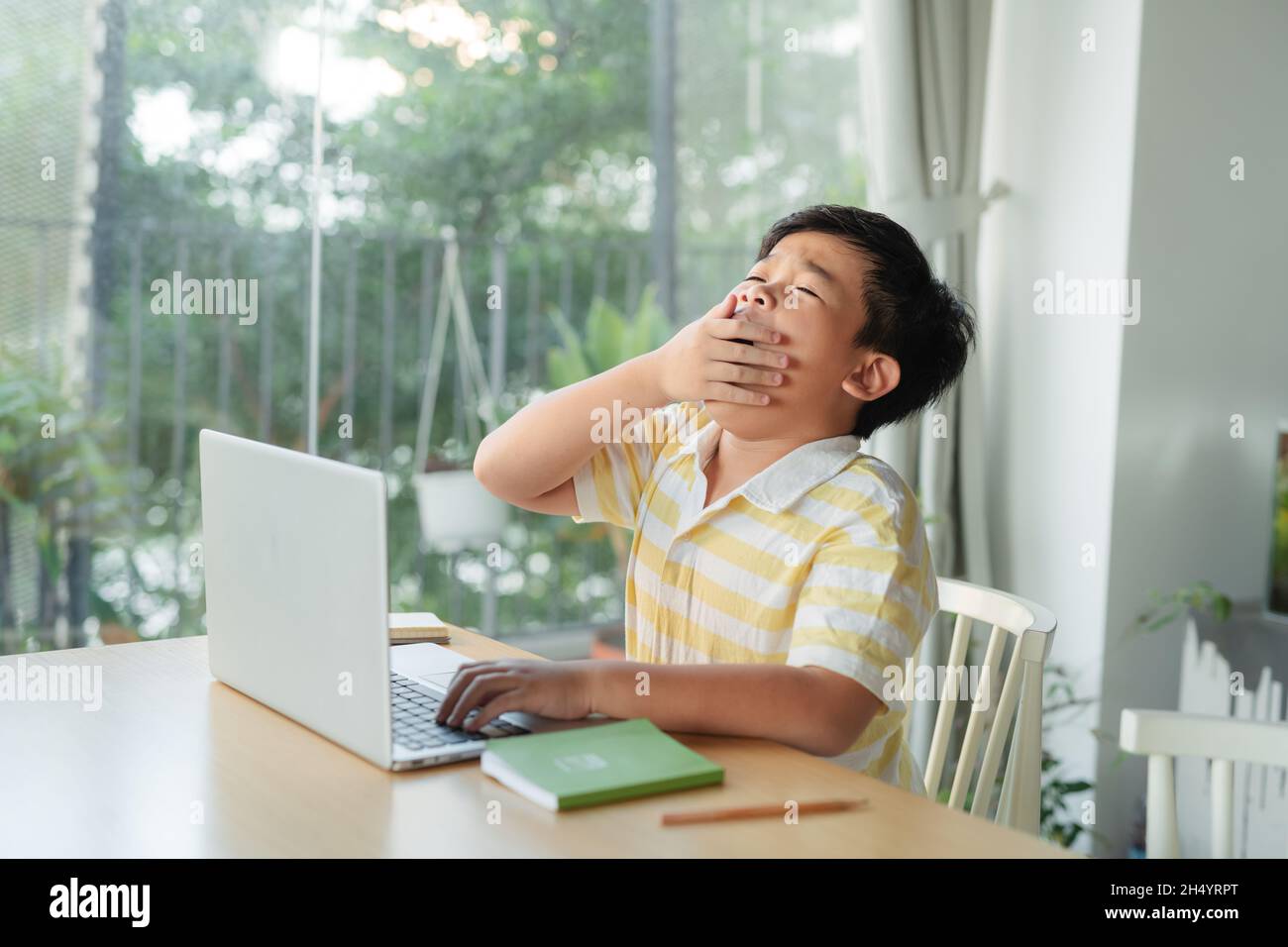 asian child sitting at a table at home with tablet laptop and to yawning Stock Photo
