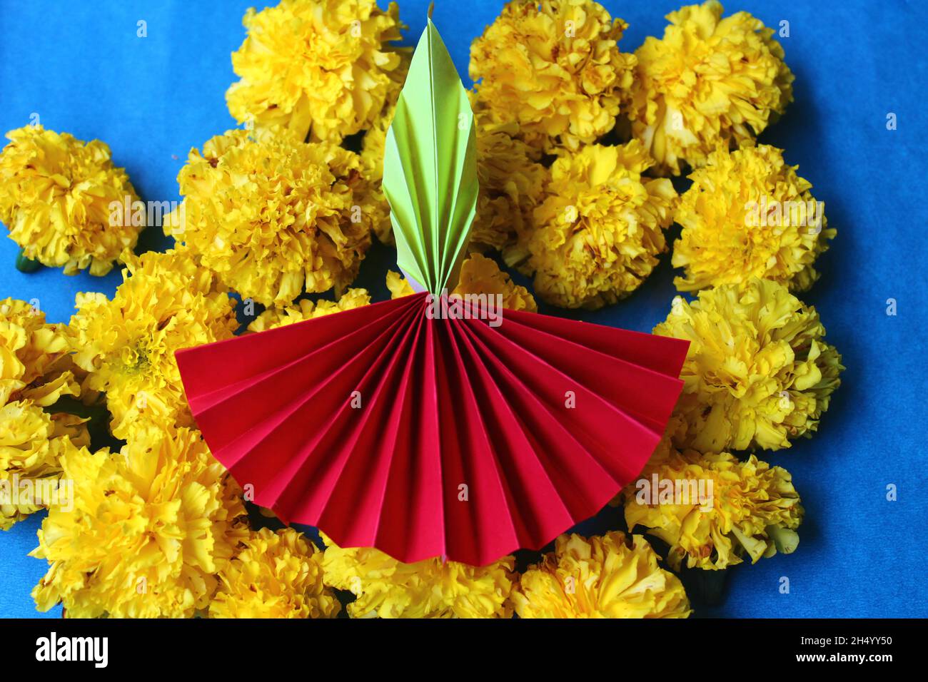 Diwali diya made with origami paper and fresh marigold flowers on blue background Stock Photo