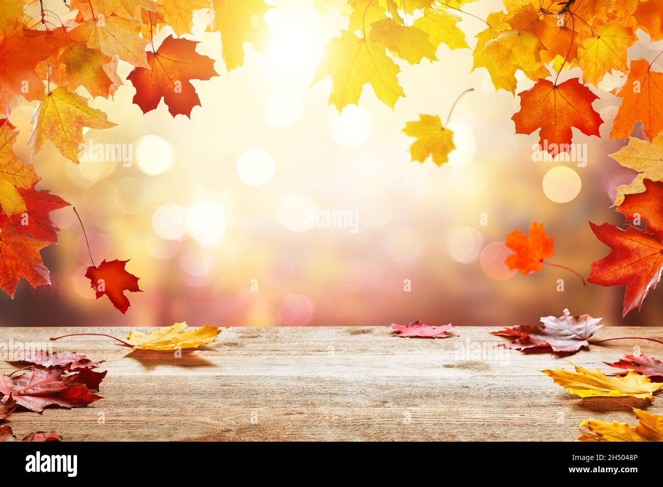 Wooden table top on blur autumn background. Autumn golden abstract background with bokeh light and colorful fall leaves. Stock Photo