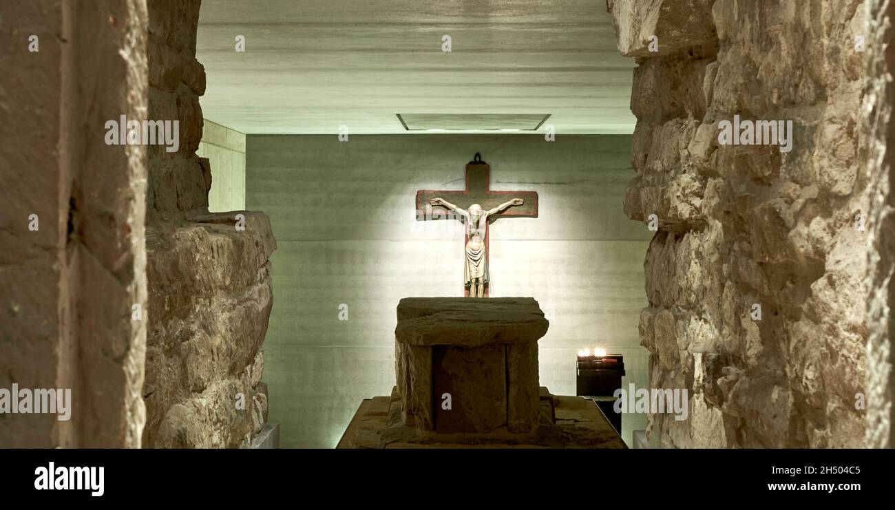 Hildesheim, Germany, November 4, 2021: Old sarcophagus in front of a modern crucifix in the crypt with illumination from candlelight Stock Photo
