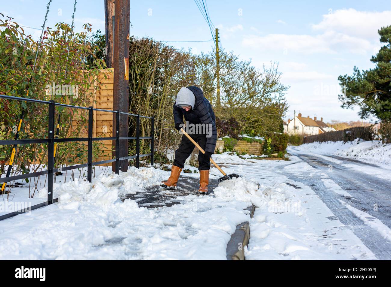 A young man clearing the footpath of snow and ice to make it safe to