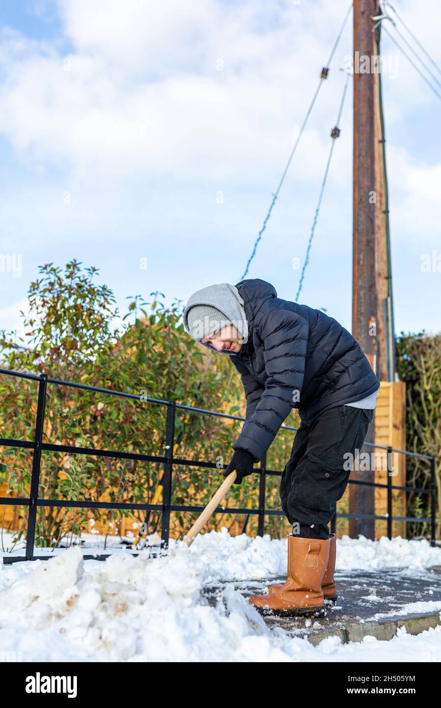 A young man clearing the footpath of snow and ice to make it safe to