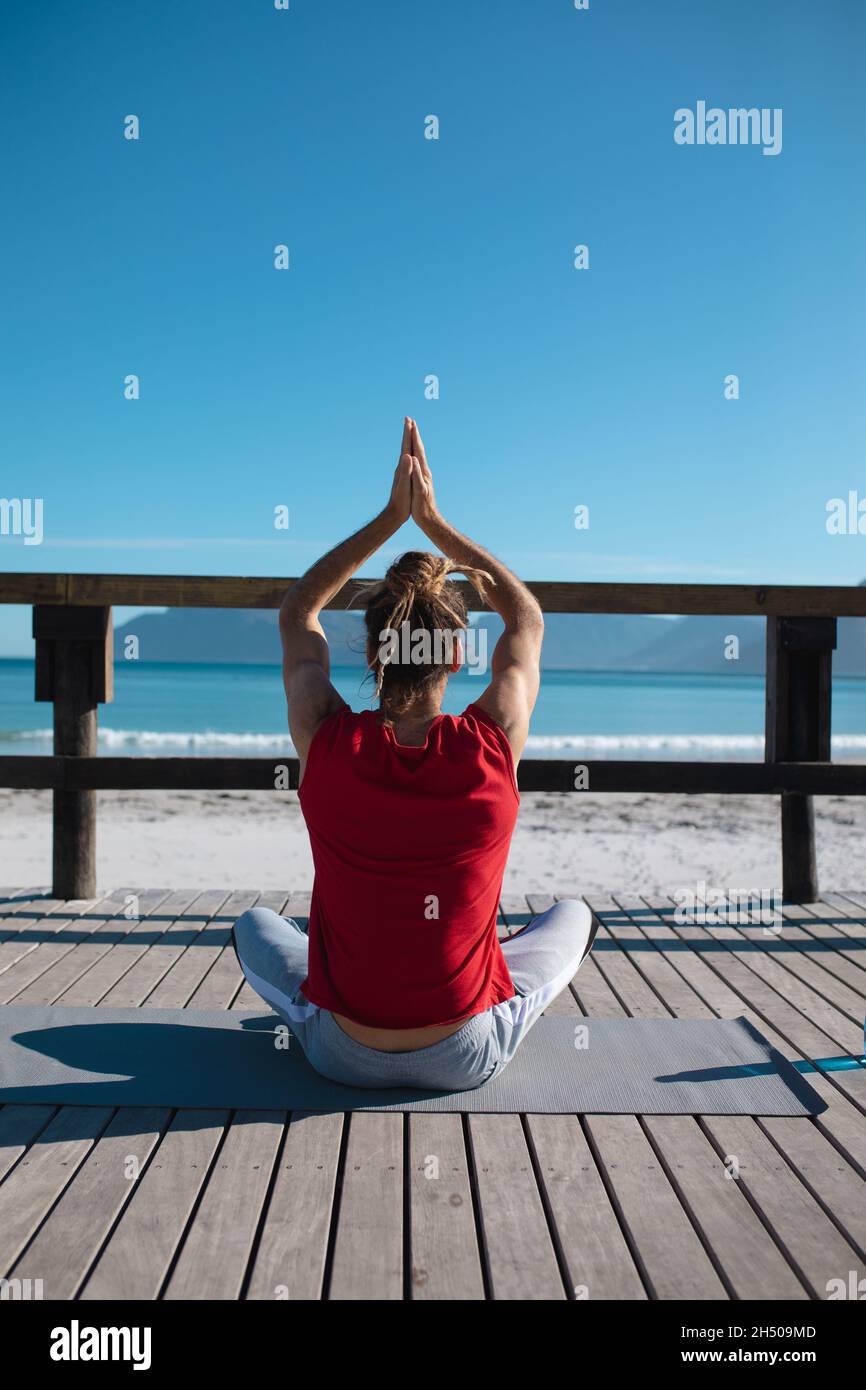 Rear view of man practicing yoga while meditating with hands clasped on floorboard, copy space Stock Photo