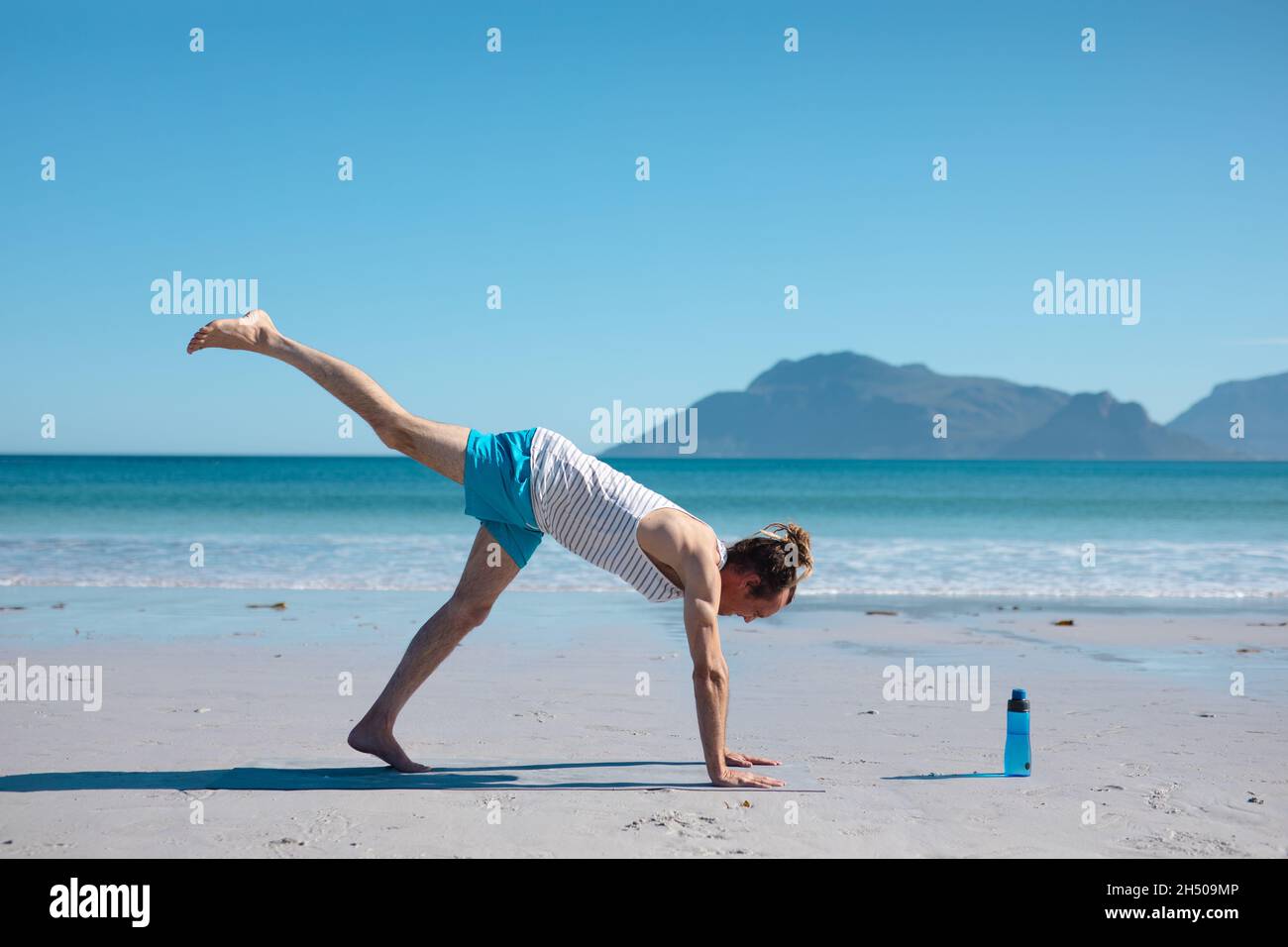 Hipster man practicing downward dog pose yoga with one leg up against blue sky and copy space Stock Photo